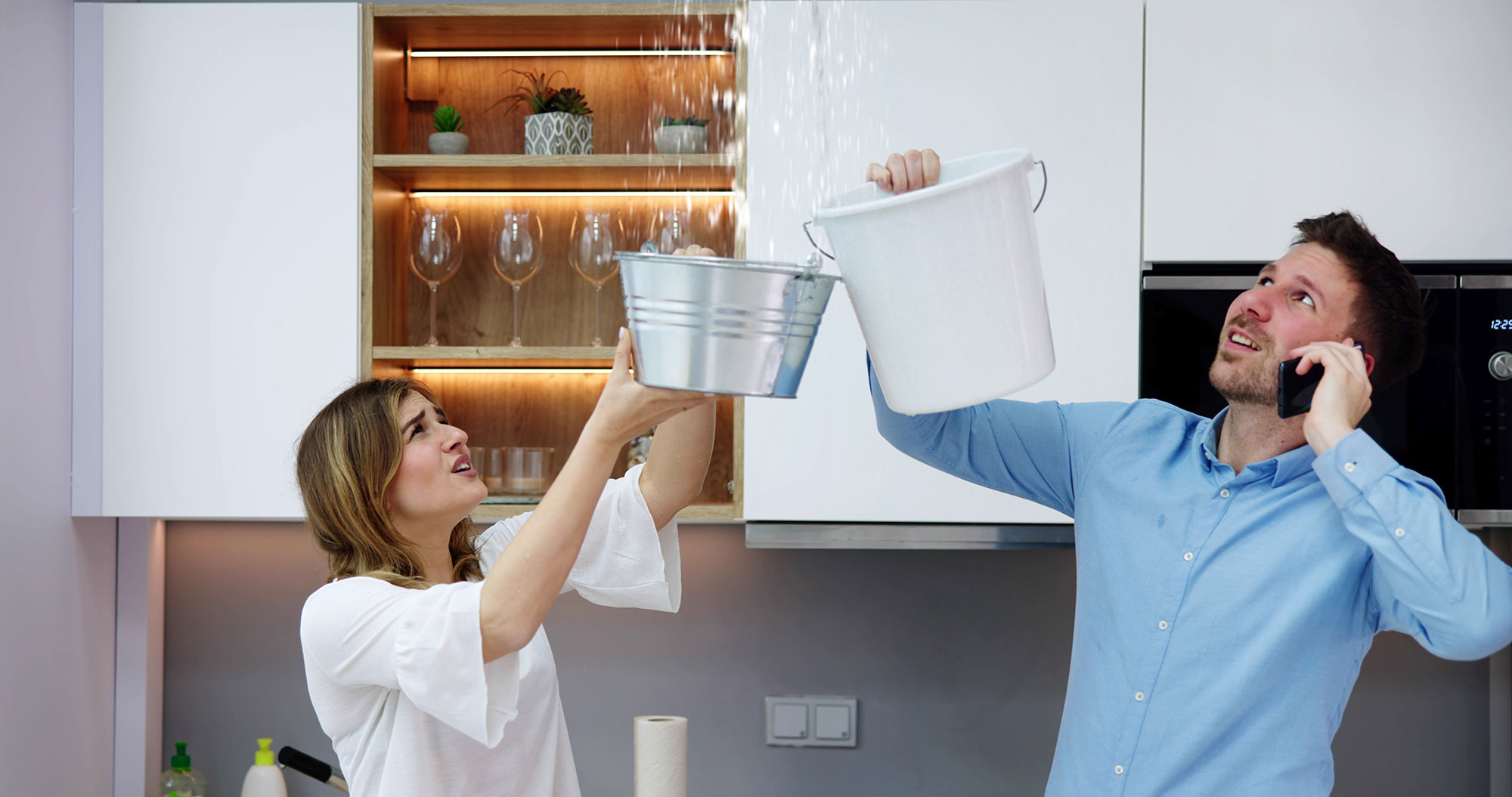 couple holding buckets to catch water coming from water leak in ceiling